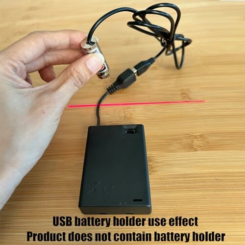 Hand holding USB battery holder with attached cable on wooden surface.